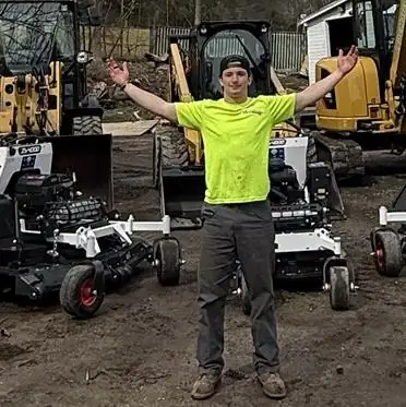 John A. DeMarco with his arms out in front of our mowers and machines
