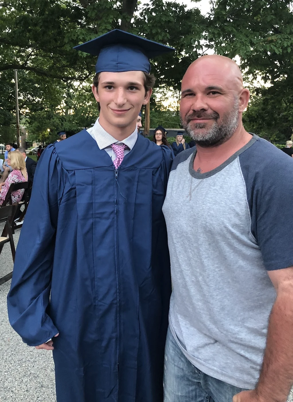 Johnny in his navy cap and gown at his high school graduation, standing beside his dad